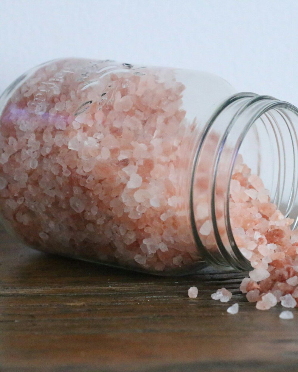 Pink bath salts spilling from a glass jar onto wood