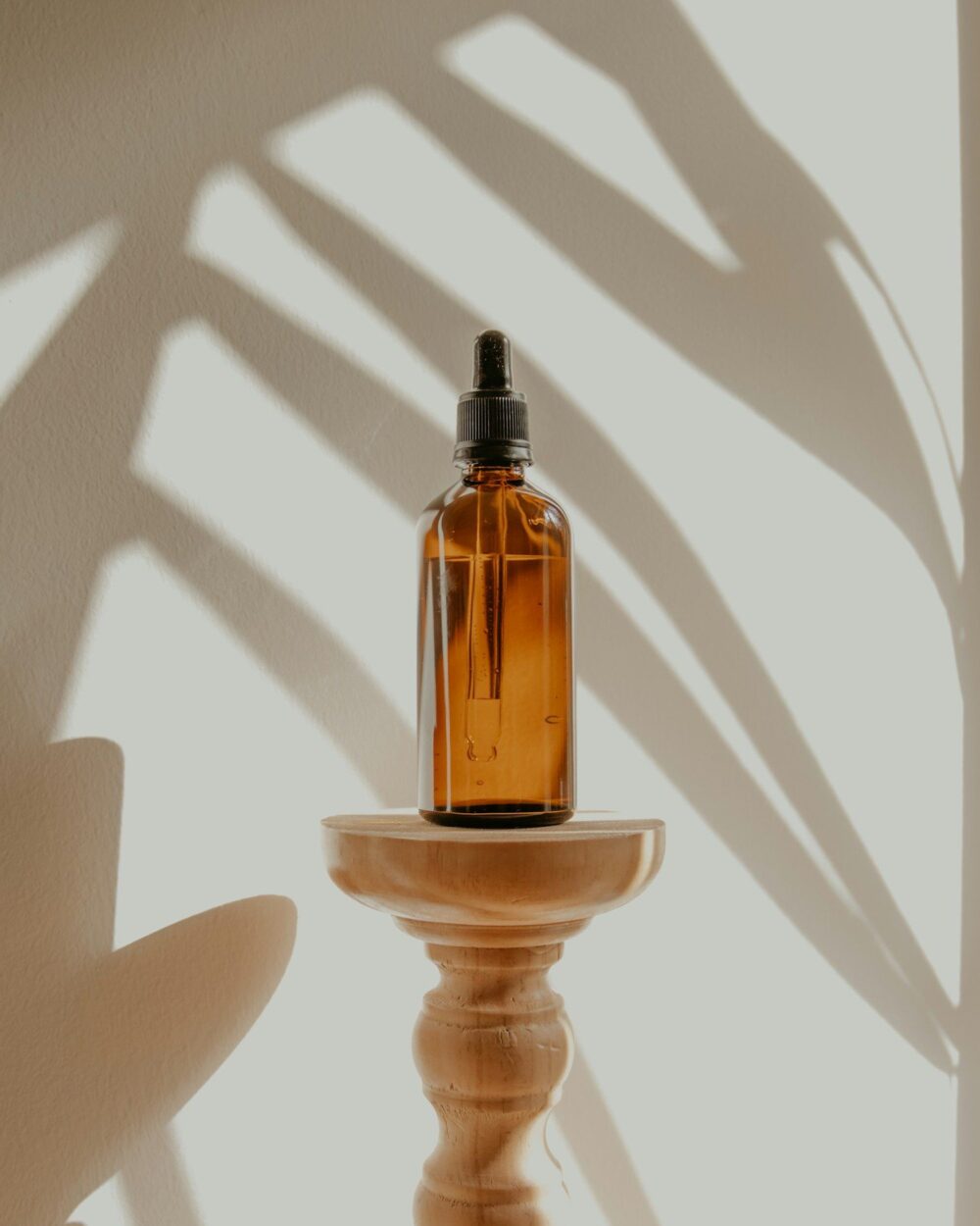 Amber dropper bottle in palm-leaf shadow