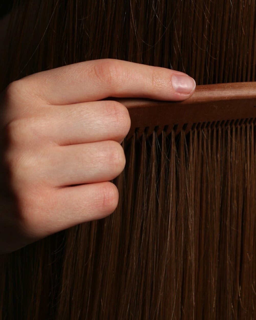 A hand drawing through dark, oiled hair